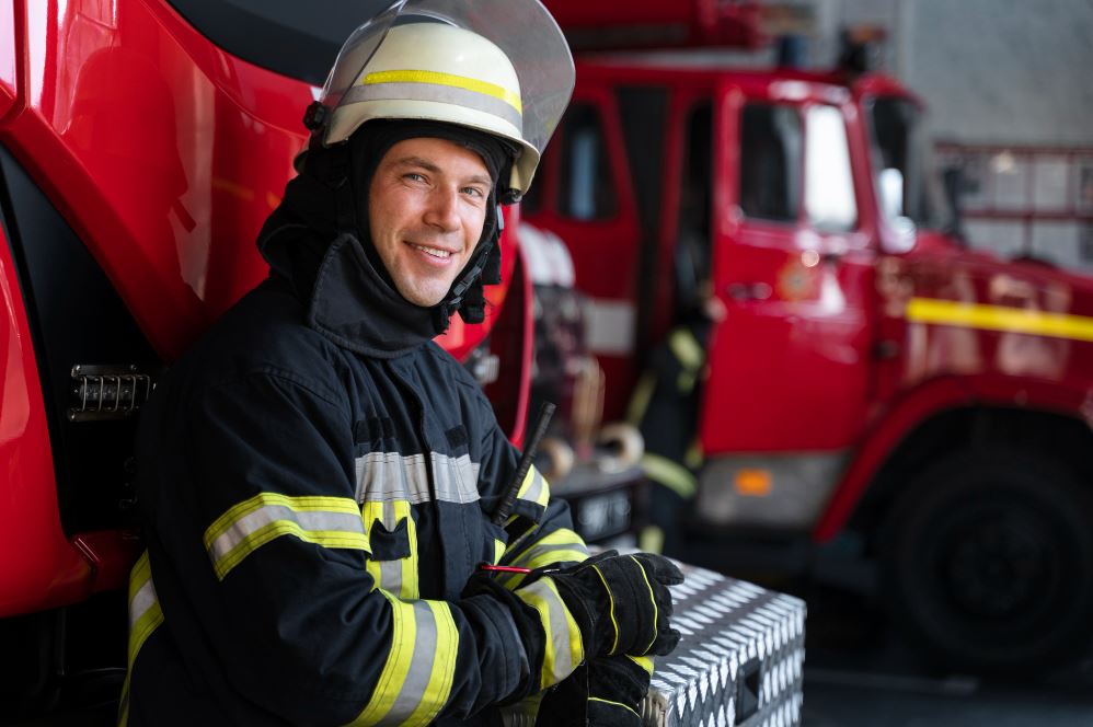 Bombero sonriendo recargado en un camión de bomberos